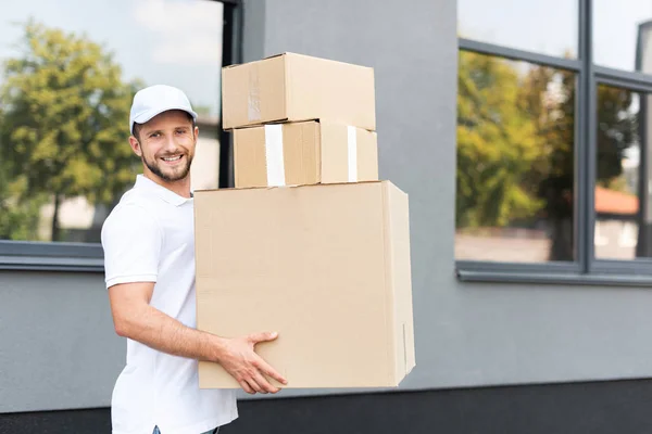 Fröhlicher Auslieferer Mit Mütze Blickt Kamera Und Hält Kisten — Stockfoto