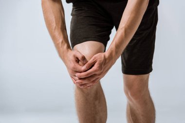 cropped view of sportsman with knee pain isolated on grey clipart