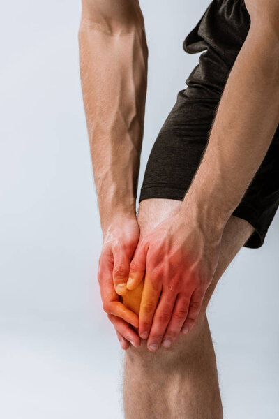 cropped view of sportsman with knee pain isolated on grey