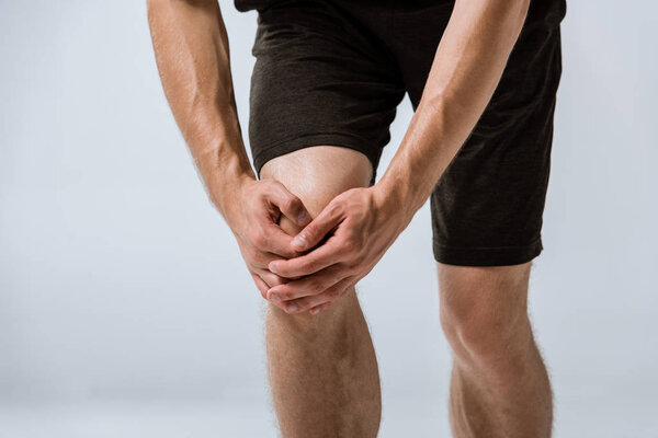 cropped view of sportsman with knee pain isolated on grey