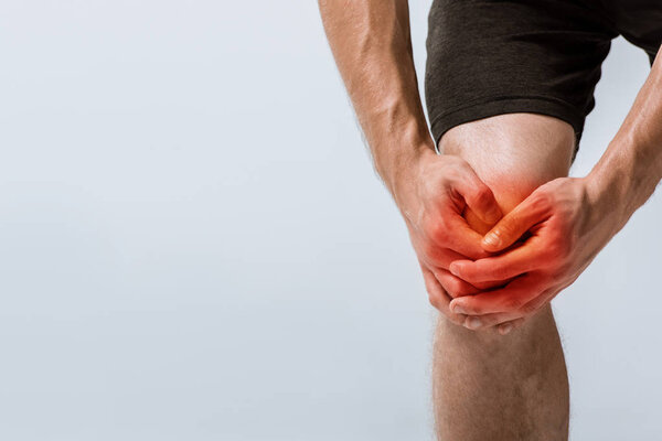 cropped view of sportsman with knee pain isolated on grey