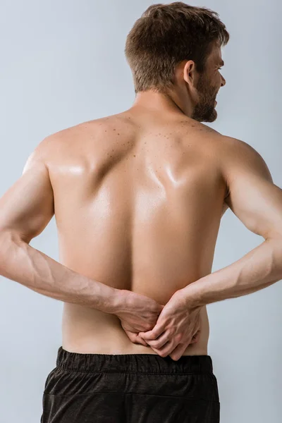 灰色で隔離された腰痛を持つシャツレススポーツマンのバックビュー — ストック写真