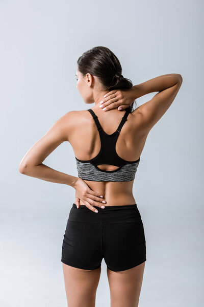 back view of sportswoman with neck pain isolated on grey