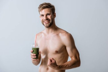 smiling shirtless sportsman holding smoothie and clenching fist isolated on grey clipart