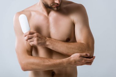 cropped view of shirtless man holding bottle of ointment and touching elbow isolated on grey clipart