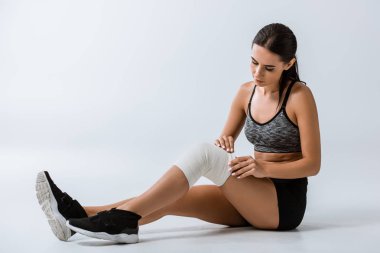 sportswoman with elastic bandage on knee sitting on grey clipart
