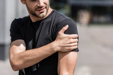 cropped view of sportsman in black t-shirt with shoulder pain on street clipart