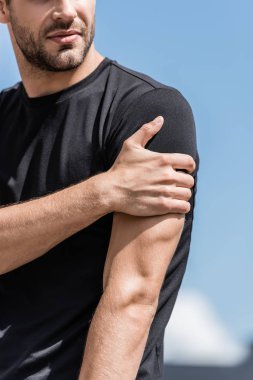 mavi gökyüzü altında omuz ağrısı ile siyah t-shirt sporcu kırpılmış görünümü