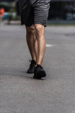 partial view of sportsman in black sneakers walking on street clipart