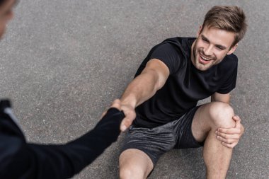 cropped view of woman helping sportsman with injured knee on street clipart