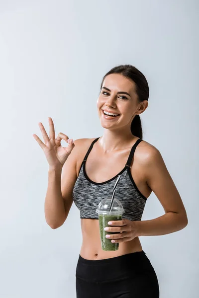 Smiling Sportswoman Holding Smoothie Showing Okay Sign Isolated Grey — Stock Photo, Image