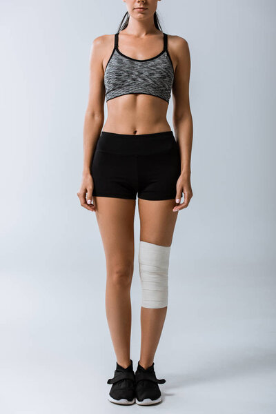 обрезанный вид спортсменки с эластичной повязкой на колене на сером
