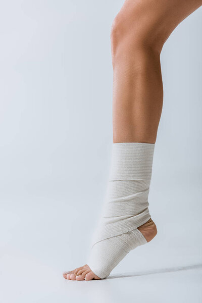 partial view of barefoot girl with elastic bandage on foot on grey