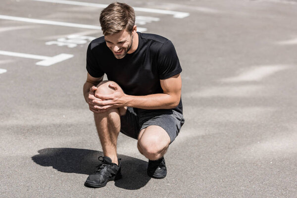 bearded sportsman in black t-shirt with knee pain on street