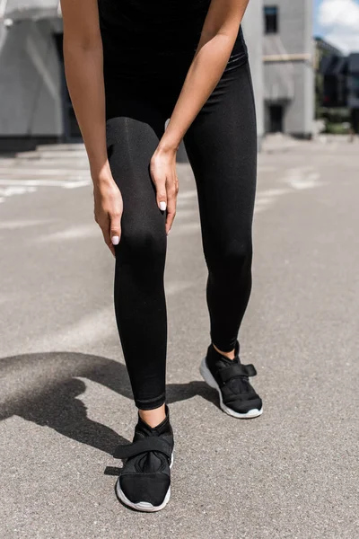 穿着黑色运动鞋的女运动员的裁剪视图与膝盖疼痛在街上 — 图库照片