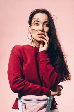 Pembe üzerine izole edilmiş kırmızı kazaklı ve bel çantalı çekici Asyalı kadın. 
