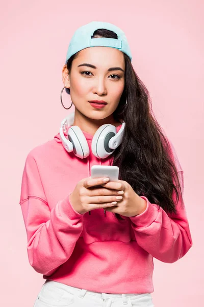 Atractiva Mujer Asiática Jersey Gorra Con Auriculares Sosteniendo Teléfono Inteligente — Foto de Stock