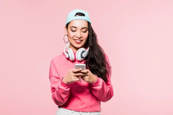 Uśmiechnięta Azjatka Pulowerze Czapce Słuchawkami Smartfonem Odizolowanym Różowo — Zdjęcie stockowe