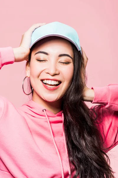 迷人的亚洲女人 紧闭双眼 身穿粉色套头毛衣 头戴一顶帽子 面带微笑 与粉色隔离 — 图库照片