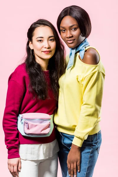 attractive asian and african american friends smiling isolated on pink