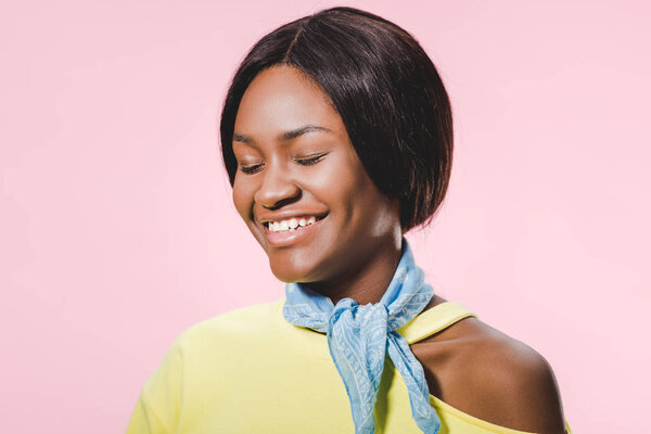 smiling african american woman in yellow pullover and scarf with closed eyes isolated on pink 
