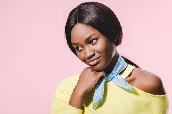 pensive african american woman in yellow pullover and scarf looking down isolated on pink 