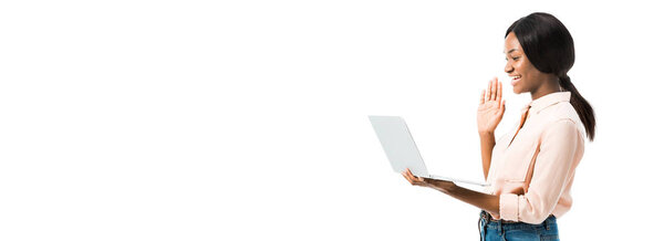 panoramic shot of african american woman in shirt holding laptop and talking in video chat isolated on white 