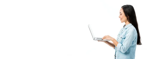 Панорамний Знімок Привабливої Азіатки Джинсовій Сорочці Посміхаючись Тримаючи Ноутбук Ізольовано — стокове фото