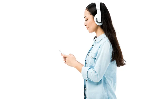 穿着牛仔衬衫 一边听音乐 一边拿着被白色隔离的智能手机的漂亮的亚洲女人的侧视图 — 图库照片