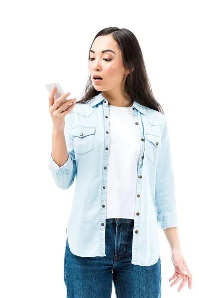白に隔離されたスマートフォンを持ったデニムシャツ姿のアジア系女性が魅力的でショックを受けた — ストック写真