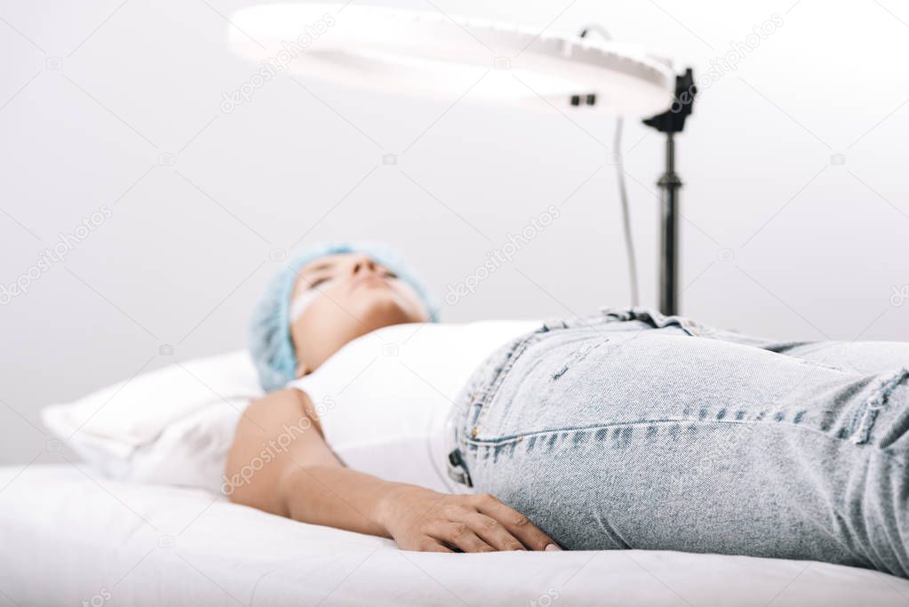 selective focus of model lying on couch under lamp isolated on grey, eyelash extensions