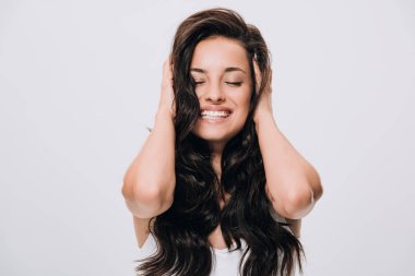happy brunette beautiful woman touching long curly healthy hair isolated on grey clipart