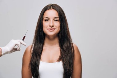 gri izole uzun saçlı esmer güzel kadın yakınında kafa derisi mezoterapi için şırınga tutan lateks eldiven kozmetolojist