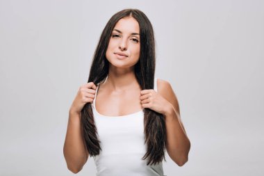 brunette beautiful woman holding long straight healthy and shiny hair isolated on grey clipart
