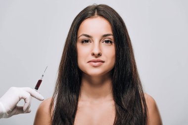 gri izole uzun saçlı esmer güzel kadın yakınında kafa derisi mezoterapi için şırınga tutan lateks eldiven kozmetolojist