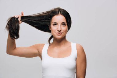 gülümseyen esmer güzel kadın gri izole uzun düz sağlıklı ve parlak saçtutarak