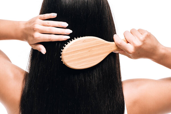 back view of brunette beautiful woman brushing long straight healthy and shiny hair with comb isolated on white