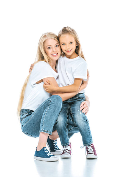 happy mother and daughter hugging and looking at camera on white