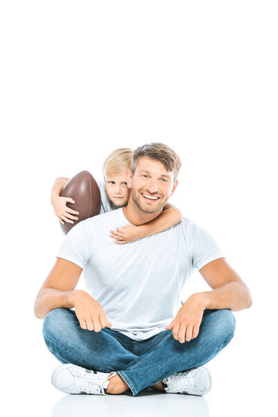 cute boy holding rugby ball and hugging happy father on white 