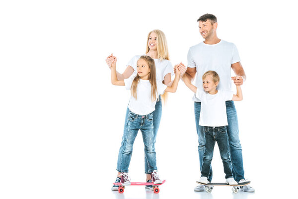 happy parents near holding hands of children riding penny boards on white 