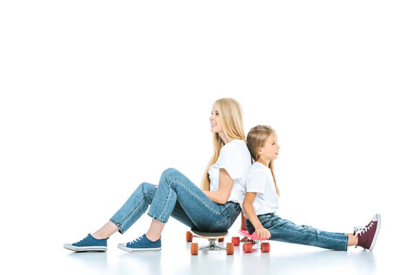 cheerful mother and positive child sitting on penny boards on white 