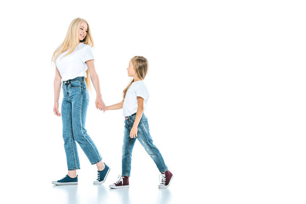 happy mother holding hands with kid and walking on white 