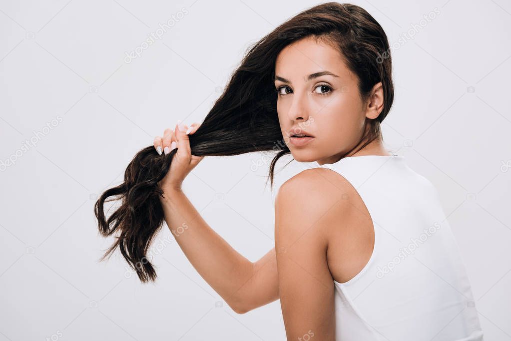 brunette beautiful woman holding long healthy and shiny hair isolated on grey