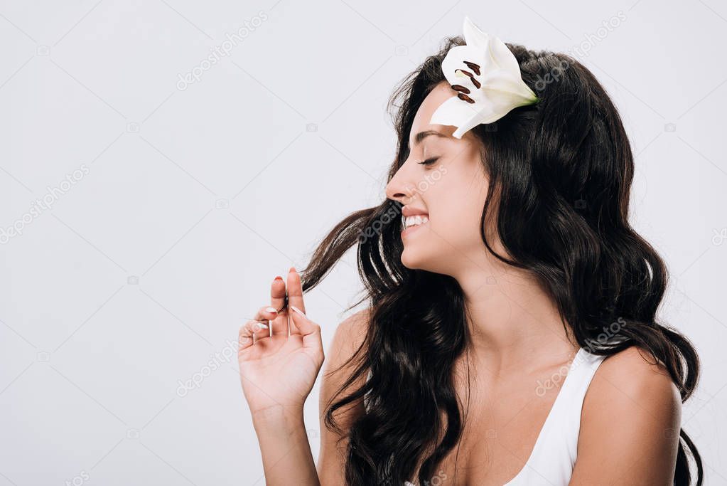 smiling brunette beautiful woman with lily in long healthy hair isolated on grey