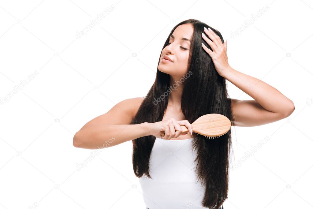 brunette beautiful woman with closed eyes brushing long straight healthy and shiny hair with comb isolated on white