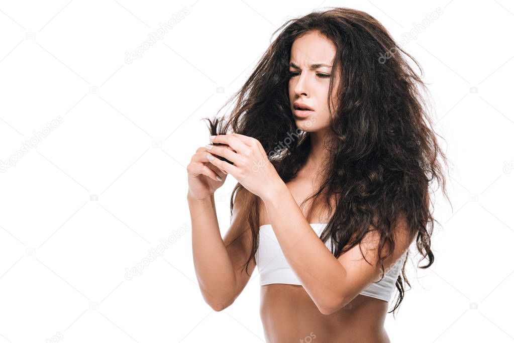 stressed brunette woman looking at damaged dry hair isolated on white