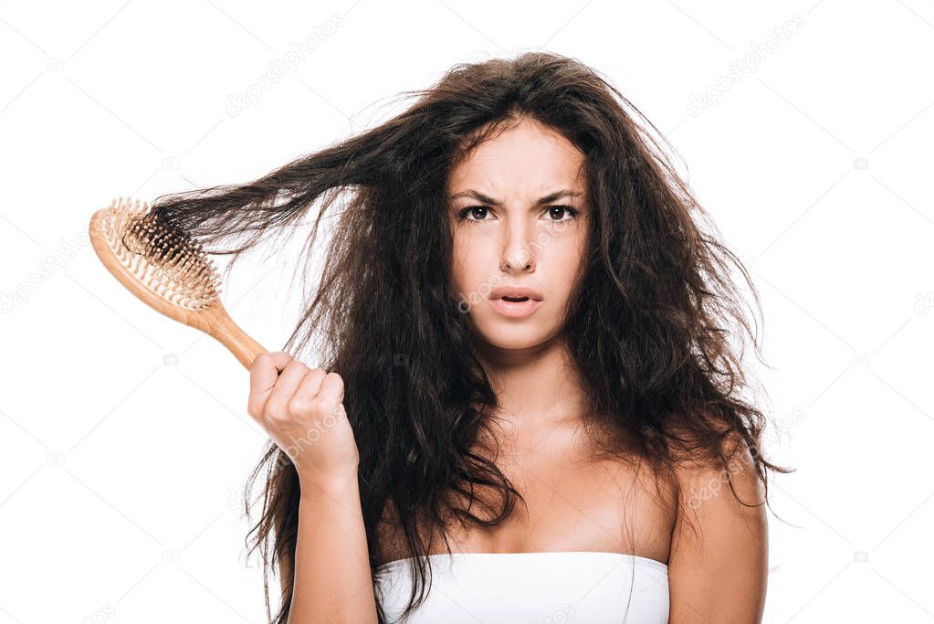 tense brunette woman holding wavy unruly hair in comb isolated on white