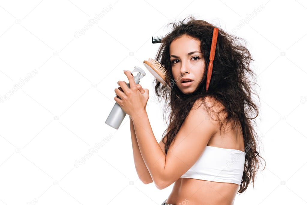 brunette woman with combs in wavy unruly hair holding spray isolated on white