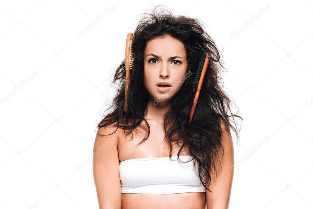 confused brunette woman with combs in wavy unruly hair isolated on white