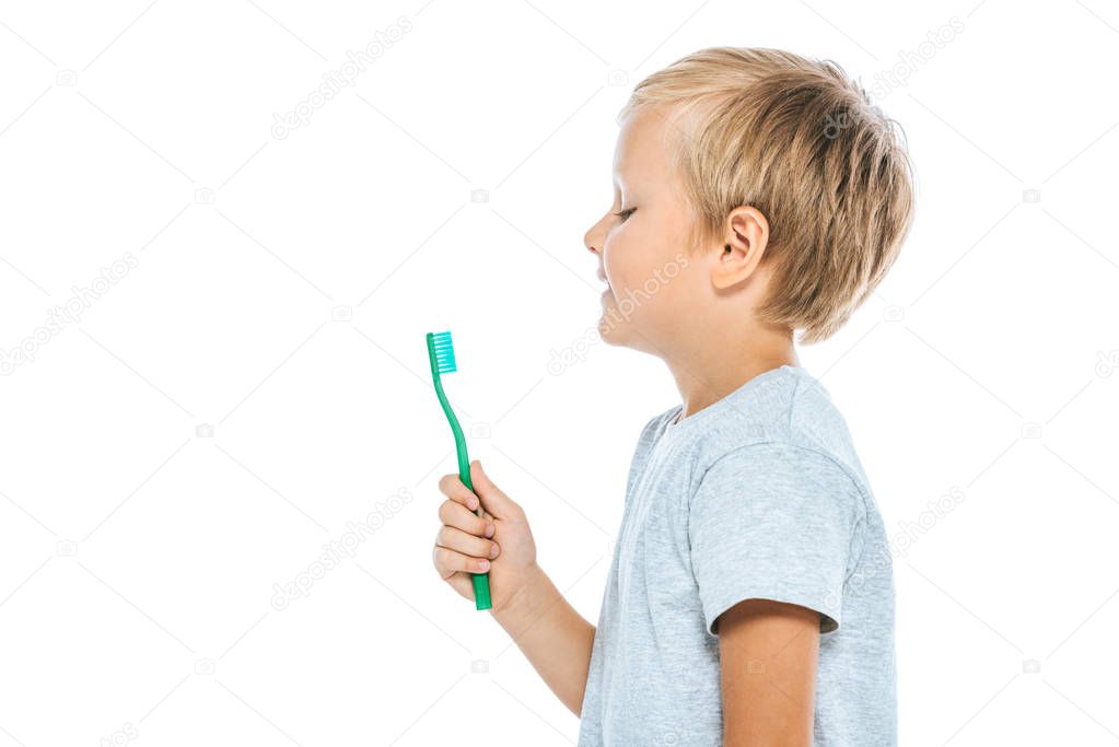 side view of happy boy looking at toothbrush isolated on white 